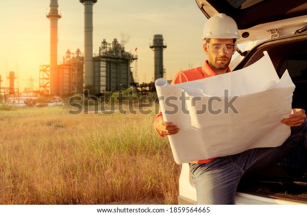male caucasian engineer\
technician Industrial workers wearing safty uniform with\
walkie-talkie and laptop working inspection in a car with power\
plant background