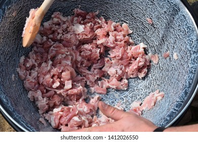 Male caucasian hands stirring a large pot of raw diced meat with oil on an outdoor cooker
