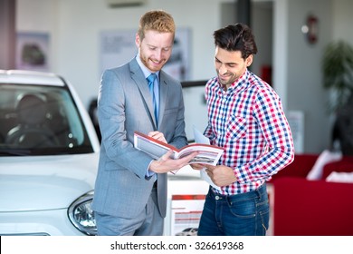 Male Caucasian salesman and male client at the car dealership saloon indoors