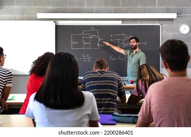 Profesora caucásica masculina explicando electrónica y física a estudiantes de secundaria multirraciales.