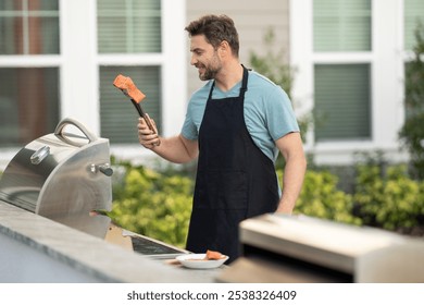 a male chef in an apron grills salmon steak with vegetables for dinner. A chef grilling fish on an open flame, preparing it with herbs and lemon. man cooking salmon on grill outdoor grill salmon fish - Powered by Shutterstock