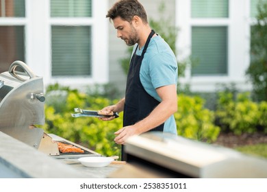 a male chef in an apron grills salmon steak with vegetables for dinner. A chef grilling fish on an open flame, preparing it with herbs and lemon. man cooking salmon on grill outdoor grill salmon fish - Powered by Shutterstock