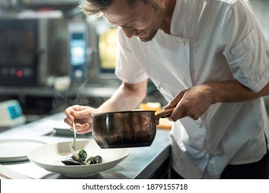 Male chef bending by kitchen table and putting boiled mussels on plate while taking them out of metallic pan before serving food to client - Powered by Shutterstock