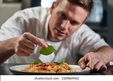 Male Chef Garnishing Plate Of Food In Professional Kitchen     