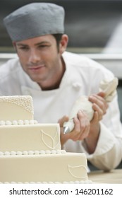 Male Chef Icing Wedding Cake In Kitchen