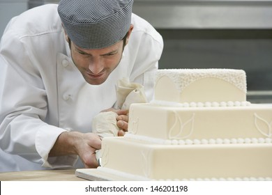 Male Chef Icing Wedding Cake In Kitchen