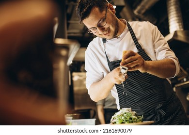 Male chef at kitchen preparing salad rubbing cheese on top - Powered by Shutterstock