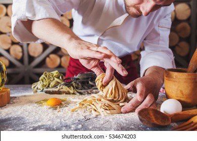 Male Chef Making Homemade Pasta With Flour And Eggs Over Old Wooden Table