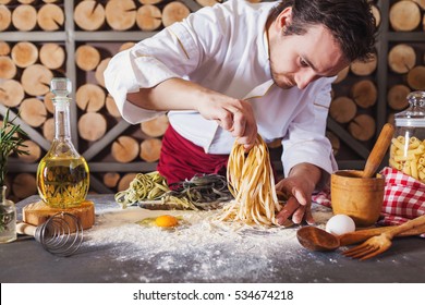 Männlicher Chefkoch, der hausgemachte Nudeln mit Mehl und Eier auf einem alten Holztisch zubereitet