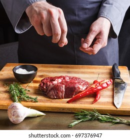 Male chef seasoning rib eye steak. Fresh meat, salt, garlic, chilli pepper and rosemary on wooden board. Modern restaurant cuisine background - Shutterstock ID 697376947