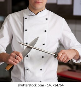 Male Chef Sharpening Knife In Commercial Kitchen