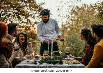 A male chef in uniform is serving a private elegant dinner to a group of people, People are smiling and welcoming the chef who is serving and bringing delicious food. - Powered by Shutterstock