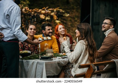 A male chef in uniform is serving a private elegant dinner to a group of people, People are smiling and welcoming the chef who is serving and bringing delicious food. - Powered by Shutterstock