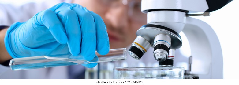 Male chemist holds test tube of glass in hand portrait overflows liquid solution potassium permanganate conducts an analysis reaction takes various versions of reagents using chemical manufacturing.