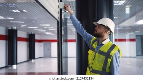 Male Chief Engineer In Hardhat And Vest Standing Inside Commercial Building Construction Site, Closing An Automatic Roller Door Before Leaving Work.