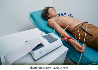 Male Child Lying On Bed During ECG Procedure With Suction Chest Electrodes. Electrocardiography For Children