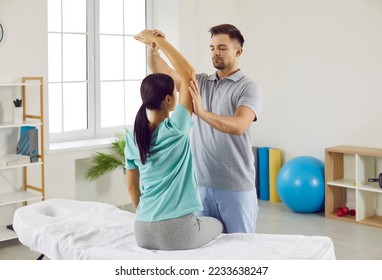 Male chiropractor, physiotherapist or osteopath at modern therapy and rehabilitation center checking womans arm. Physiotherapy specialist working with female patient whos sitting on examination bed - Powered by Shutterstock