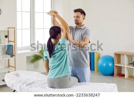 Male chiropractor, physiotherapist or osteopath at modern therapy and rehabilitation center checking womans arm. Physiotherapy specialist working with female patient whos sitting on examination bed