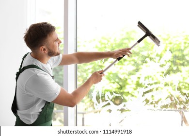 Male Cleaner Wiping Window Glass With Squeegee Indoors