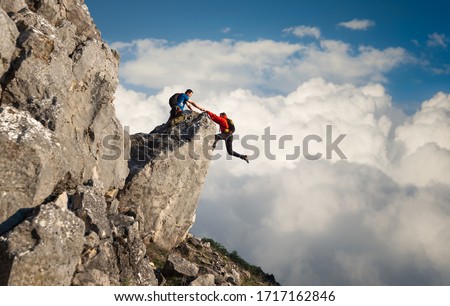 Male climber reaching out to help his friend get over the cliffs edge 