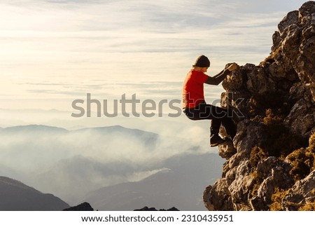 male climber in red clothes climbing a rock without a rope or safety measures to reach the top of a mountain. risky sport. adventure