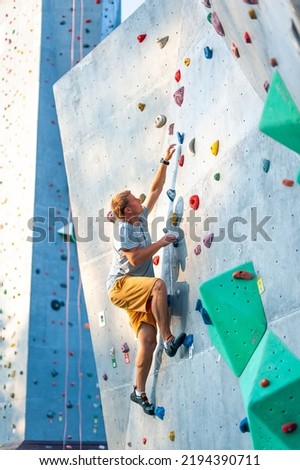 A male climber is rock climbing outdoors on an artificial boulder without a safety harness.