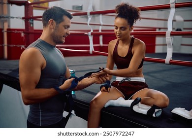 Male coach assisting sportswoman in wrapping bandages on her hands while preparing for boxing training in health club.  - Powered by Shutterstock