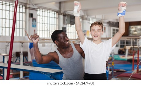 Male coach trainer and teenage athlete exulting sporting achievements at acrobatic hall - Powered by Shutterstock