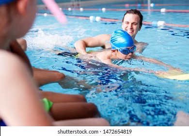 Male Coach In Water Giving Group Of Children Swimming Lesson In Indoor Pool - Powered by Shutterstock