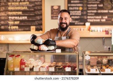 male coffee shop owner near showcase with cakes and desserts in his cafe, work in the bar cafeteria - Shutterstock ID 2176378209