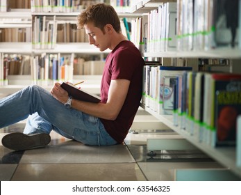 Male College Student Sitting On Floor In Library, Reading Book. Horizontal Shape, Side View, Three Quarter Length, Copy Space