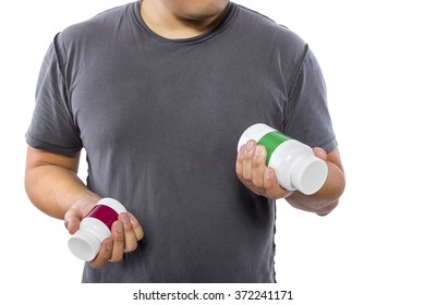 Male Comparing Bottles Of Medicine Or Dietary Supplements.  He Is Holding Two Pill Bottles With Copyspace For Logos.  The Image Can Depict Medicine Versus Generic Drug Brands. 