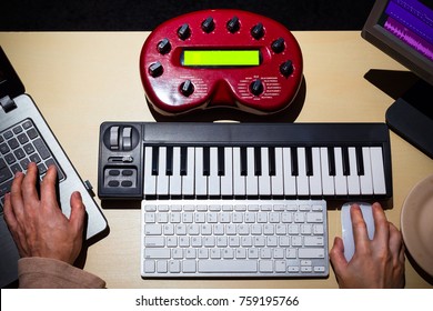 male composer hands using computer, midi keyboard & studio equipment making songs and sound design on desk for post production or music score on film