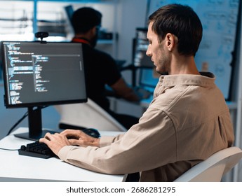 Male Computer Programmer working on Computer Writing and Developing Software Program and App looking at Dual screens in Creative Office workspace. Focused Professional male software developer work.