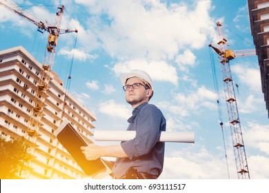 Male construction builder worker - foreman is engineer in protective helmet,glasses on the background of building a house with a crane.