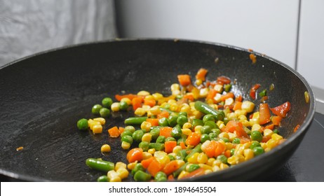 Male Cook Holding Frying Pan And Tossing Up Mixed Vegetables At Kitchen Restaurant. Chef Throwing Up Corn, Peas, Asparagus, Pepper And Carrot On Skillet At Cuisine. Concept Of Cooking Food. Slow Mo