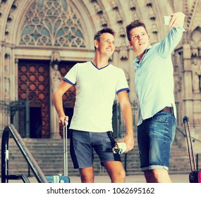 Male couple with luggage doing selfie at travel destination background