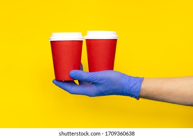 Male Courier Hand In Medical Gloves Holding Paper Two Cups Coffee For Take Away Isolated. Contactless Delivery Service In Quarantine Coronavirus Pandemic. Delivery Man Make Volunteer Donation. Mock Up