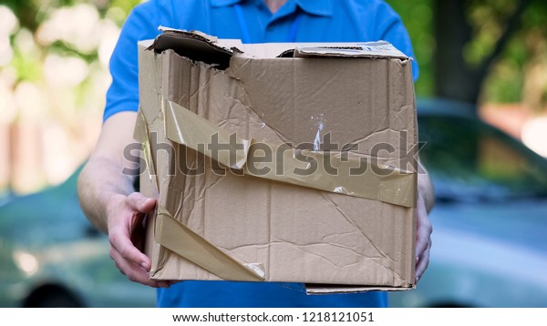Male courier showing damaged box, cheap parcel\
delivery, poor shipment\
quality