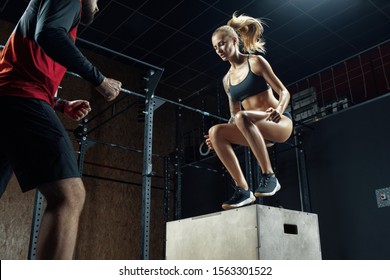 Male Crossfit Coucher Motivating Woman On Her Workout Routines. Sporty Girl And Man Workout Box Jump Crossfit Routine At The Gym. Young Fitness Woman With Man Crossfit Workouts 