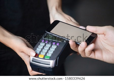 Male customer buyer make payment holding mobile phone above nfc terminal, consumer pay with cellphone concept, cashier use modern machine for contactless smartphone transaction service, close up view