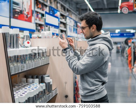 male customer buying spray paint can in the supermarket. He is reading what to buy. difficult decision. Various choice