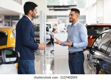 Male Customer Choosing New Car At Luxury Auto Dealership Salon, Young Middle Eastern Man Having Conversation With Sales Manager At Showroom, Buying New Automobile, Side View