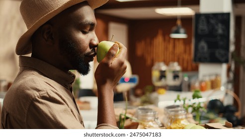 Male customer enjoying fresh smell of green apples in crates, choosing to buy fruits and veggies from local zero waste eco store. Young adult smelling natural organic aroma of produce. Camera 2. - Powered by Shutterstock