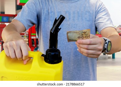 Male customer holds gallon of spare fuel refuels with diesel and holds cash to spend on expensive gas. Purchasing station services out of necessity at high cost of living and inflation.