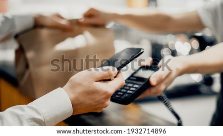 A male customer pays the bill via a smartphone using NFC technology in a cafe. Mobile phone with contactless technology. Close-up of a mobile payment hand in a cafe.