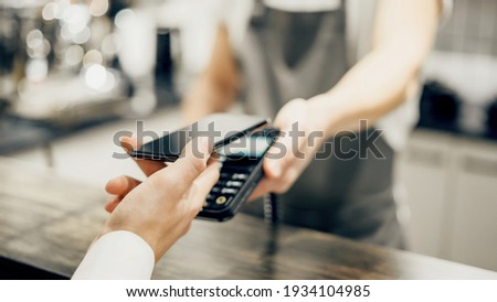 A male customer pays the bill via a smartphone using NFC technology. Take-out coffee with you. A mobile phone with contactless technology in a restaurant.