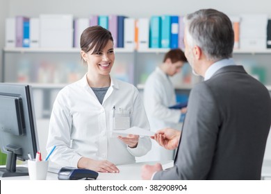 Male customer at the pharmacy, he is giving to the smiling pharmacist a prescription, healthcare concept - Powered by Shutterstock