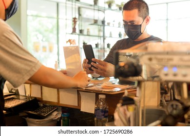 Male Customer With Protective Mask Paying Bill By Cell Phone In Cafe.