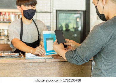 Male Customer With Protective Mask Paying Bill By Cell Phone In Cafe.